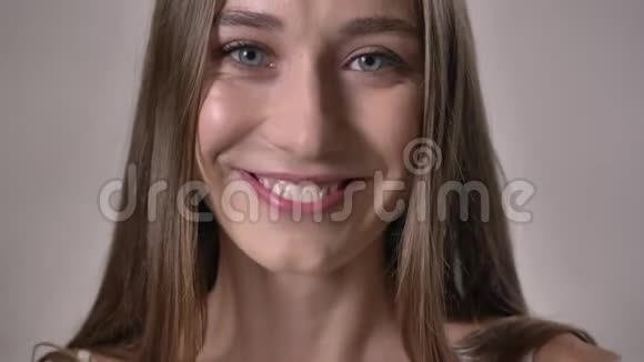 年轻开朗的女孩看着镜头微笑着抚摸着头发灰色的背景视频的预览图