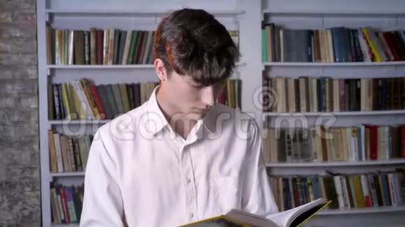 布鲁内特曼正在看书在镜头前看微笑着在后台看图书馆视频的预览图