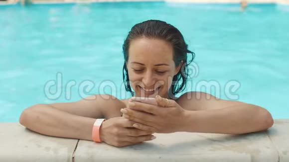 年轻女子在游泳池里使用智能手机视频的预览图