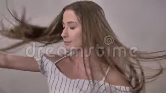 年轻迷人的女孩正在跳舞抚摸头发看镜头微笑调情的概念灰色背景视频的预览图