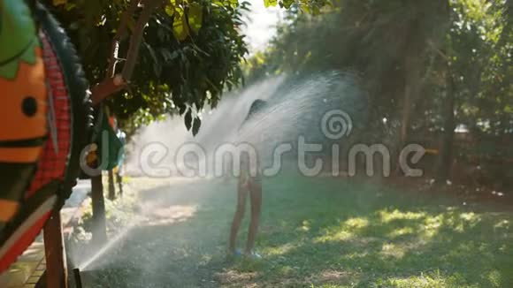 一个快乐的小女孩站在草坪浇水系统下视频的预览图