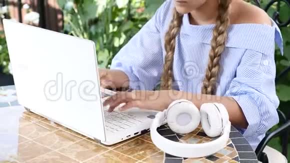 用白色笔记本电脑打字的漂亮女孩的肖像耳机在桌子上4k视频的预览图