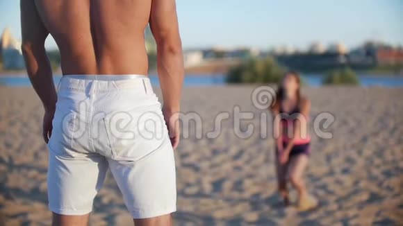 在前景中一个漂亮的运动男子赤裸的躯干穿着白色短裤从后面可以看到女孩视频的预览图