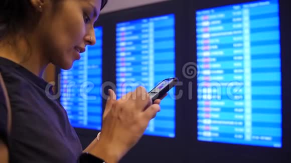 在机场离港委员会附近年轻的混血旅游女孩用手机检查她的飞行时间4K慢动作曼谷视频的预览图
