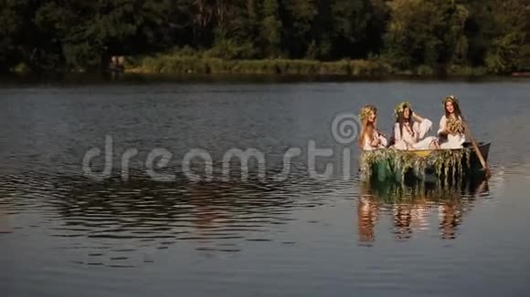 三个留着长发的小女孩坐在漂浮在河上的小船上穿着斯拉夫服装的女孩头上戴着花环视频的预览图
