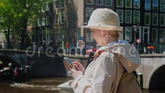 一位旅游妇女在阿姆斯特丹市中心使用智能手机在背景下船只的密集移动视频的预览图
