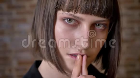 年轻体贴的女人绿色的眼睛触摸她的嘴唇看着相机和侧面砖背景视频的预览图