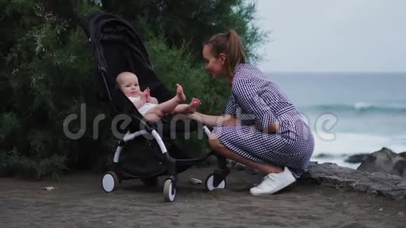 年轻母亲推着婴儿车在夏季海滩背景下的侧景视频的预览图