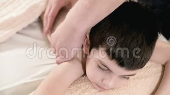 特写男理疗师按摩师为躺在按摩床上的小男孩做一个疗愈放松的按摩回去视频的预览图