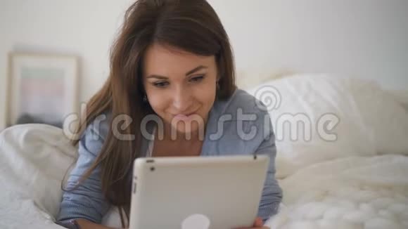 年轻女子躺在床上躺着白色床单在社交网络中聊天视频的预览图