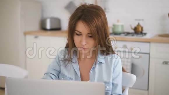 年轻女性棕色头发在明亮的厨房里用笔记本电脑工作视频的预览图