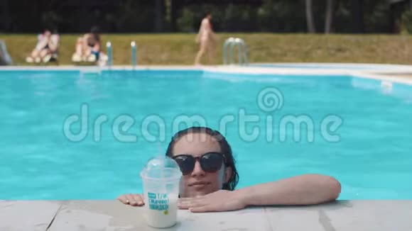 美丽的年轻女子在游泳池里游泳喝着奶昔视频的预览图