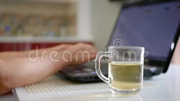 一杯茶站在笔记本电脑背景上的桌子特写上一个女人在笔记本电脑上工作拿一杯视频的预览图