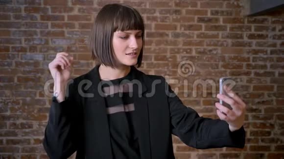 年轻的美女短发自拍摸她的头发孤立在砖背景上视频的预览图