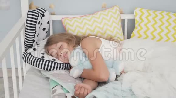 可爱的小女孩和泰迪熊睡在家里的床上视频的预览图