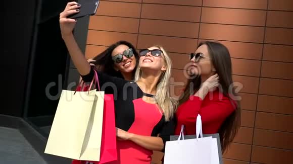 穿裙子的女孩三个迷人的年轻女孩拿着购物袋路过商店附近女孩们在笑视频的预览图