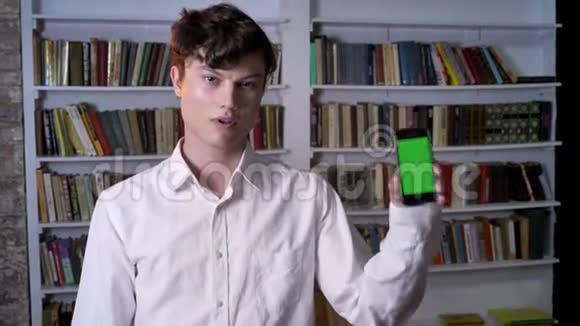 布鲁内特曼正在展示智能手机的绿色屏幕如标牌摄像头观看通讯概念图书馆等视频的预览图