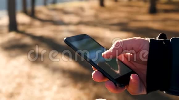 男子双手特写在秋林或公园的背景下正拿着手机一个男人在他的智能手机上工作视频的预览图