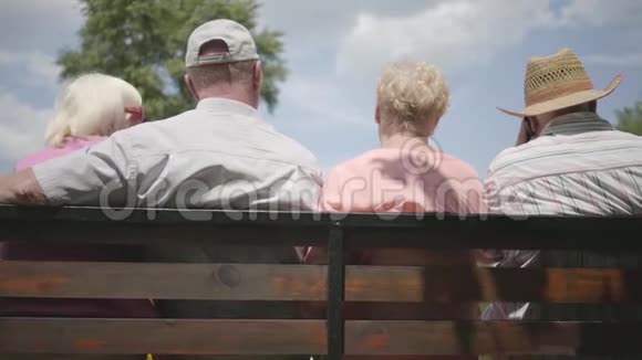 两对可爱的成年夫妇坐在长凳上一起聊天成熟的人在户外休息资深人士视频的预览图