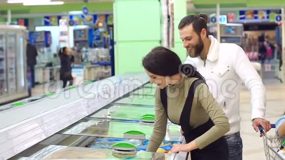 可爱的白种人夫妇从超市冰箱里选择冷冻食品视频的预览图