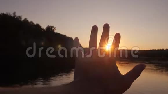 人类的手向太阳伸出阳光透过手指照射美丽的扎克特夏天在河上慢动作视频的预览图
