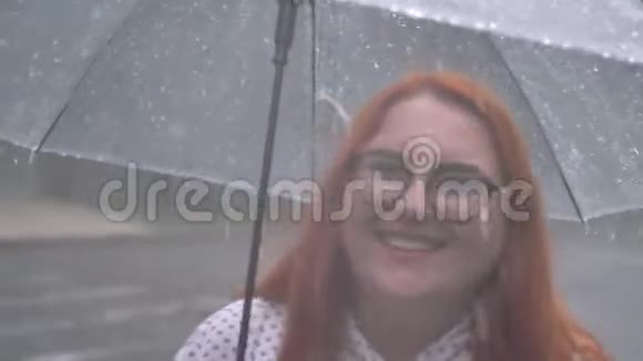 戴着眼镜的肥姜女孩在雨中漫步在公园里撑着伞看着镜头微笑着视频的预览图