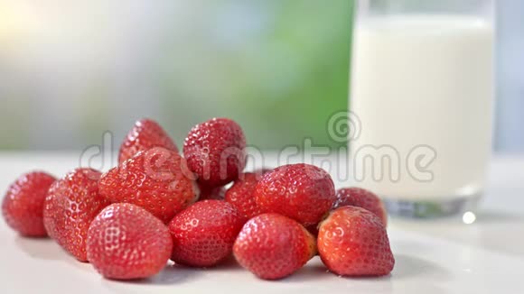 在夏季背景特写镜头中几乎没有一个环保的真正的红色草莓靠近大杯牛奶视频的预览图