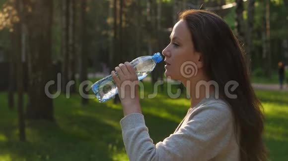 女人在傍晚的阳光下在公园喝水视频的预览图