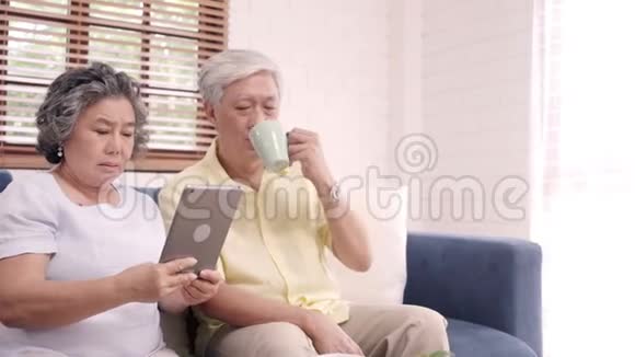 亚洲老年夫妇使用平板电脑在家客厅喝咖啡夫妇享受爱情时刻视频的预览图