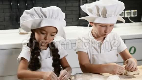 一起做饭两个孩子戴着厨师帽在家厨房里擀面两个孩子玩餐馆4k视频的预览图