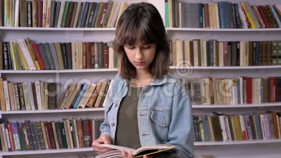 年轻的黑发女孩正在打字看书在镜头前看在后台看图书馆视频的预览图
