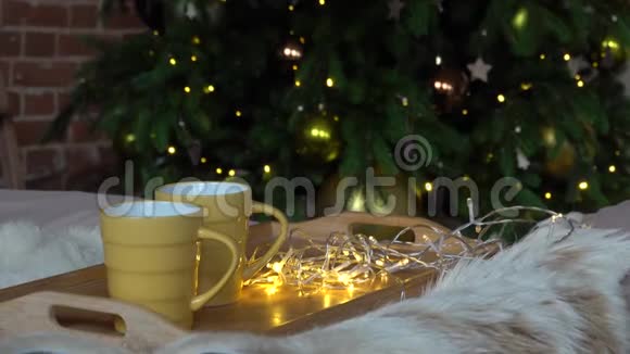 舒适的圣诞构图两个黄色的杯子上面放着热饮料一个木托盘床上放着一条蓬松的毯子视频的预览图