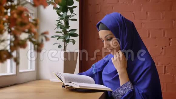穿着蓝色头巾看书的年轻美女坐在咖啡馆里迷人的女士穿着刺鼻视频的预览图