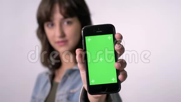 年轻的黑发女孩展示了绿色的智能手机屏幕相机观看交流概念白色背景视频的预览图