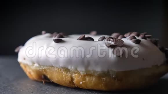 特写镜头围绕着在灰色桌子上缓慢旋转的巧克力片的美味的釉面白甜甜圈视频的预览图