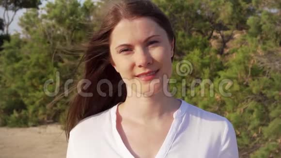 站在绿色公园里的年轻女子快乐微笑的画像风缓慢地吹着她的头发视频的预览图