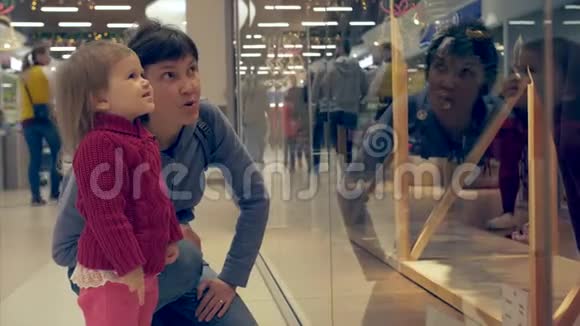 微笑的小女孩和女人指着商场的橱窗视频的预览图