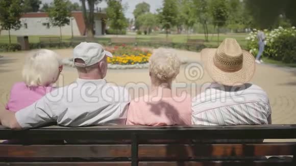 两对可爱的成熟夫妇坐在长凳上一起聊天成熟的人在户外休息资深人士视频的预览图