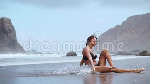 一位在海洋上从事体操的妇女坐在绳子上在水面附近的一座桥上背着海浪视频的预览图