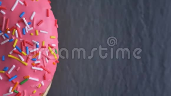 特写半镜头的粉红色甜甜圈与多色芯片和眼睛旋转缓慢的灰色桌子背景视频的预览图