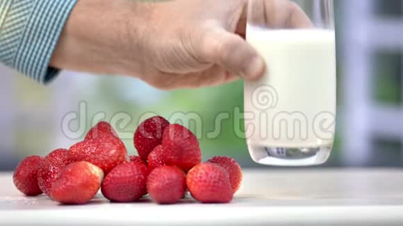 成熟男性手的特写镜头在靠近一把生态草莓的桌子上放一杯新鲜牛奶视频的预览图