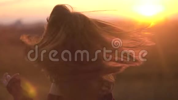 女孩在夏天的田野里摇头发美丽的女人在夕阳下摇着头发视频的预览图