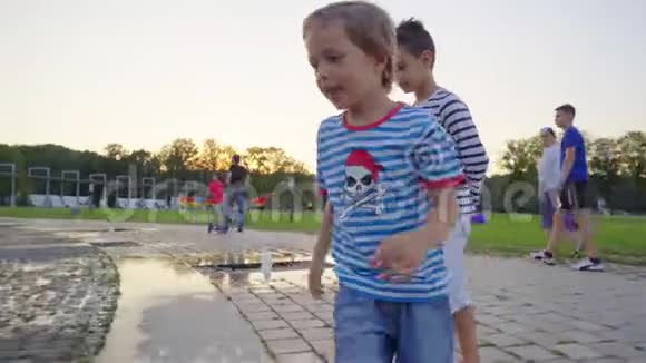 夏天晚上一个穿着牛仔短裤和黄色鞋子的小男孩在喷泉里奔跑视频的预览图
