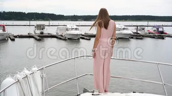 一个穿着裙子的漂亮女孩站在码头上其他船只的背景上的一艘船上转身视频的预览图