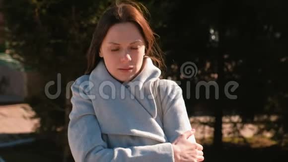 疲惫的冻僵的女人在春天的公园里等着一个人被风裹着一件外套视频的预览图