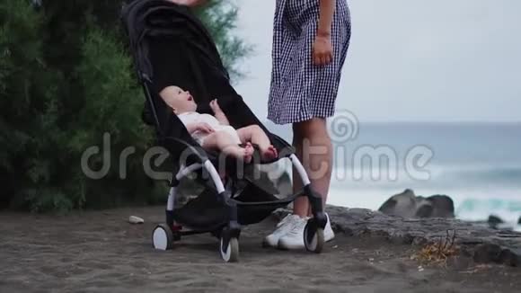 年轻母亲推着婴儿车在夏季海滩背景下的侧景视频的预览图