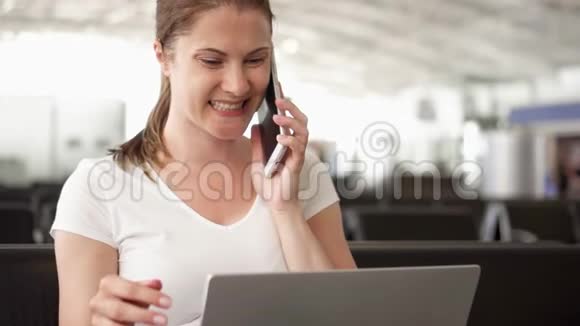 女人坐在机场候机室里拿着笔记本电脑临时女商人与同事在手机上交谈视频的预览图