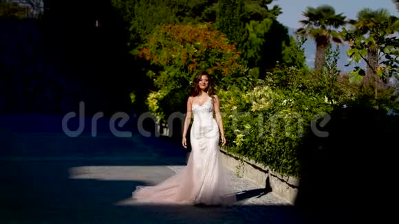 一位穿着白色裙子的新娘沿着阳光明媚的小巷走着视频的预览图