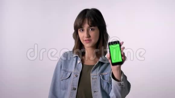 年轻的黑发女孩点在绿色的智能手机屏幕上看着相机交流理念白色背景视频的预览图