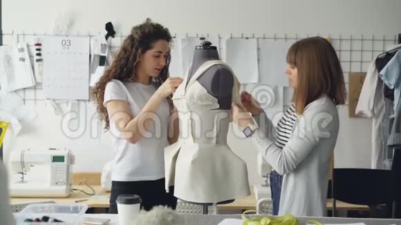 有创意的时装设计师们正在把剪裁好的布料钉在人体模型上同时用现代服装缝制女性服装视频的预览图
